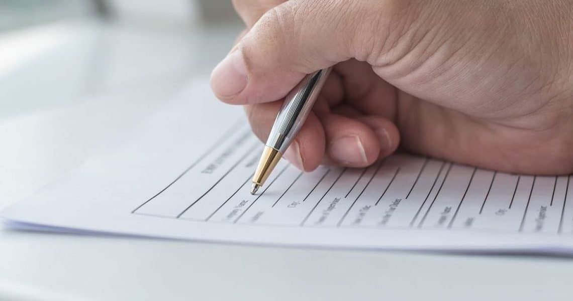 Person filling out a contractor license application form with a pen.